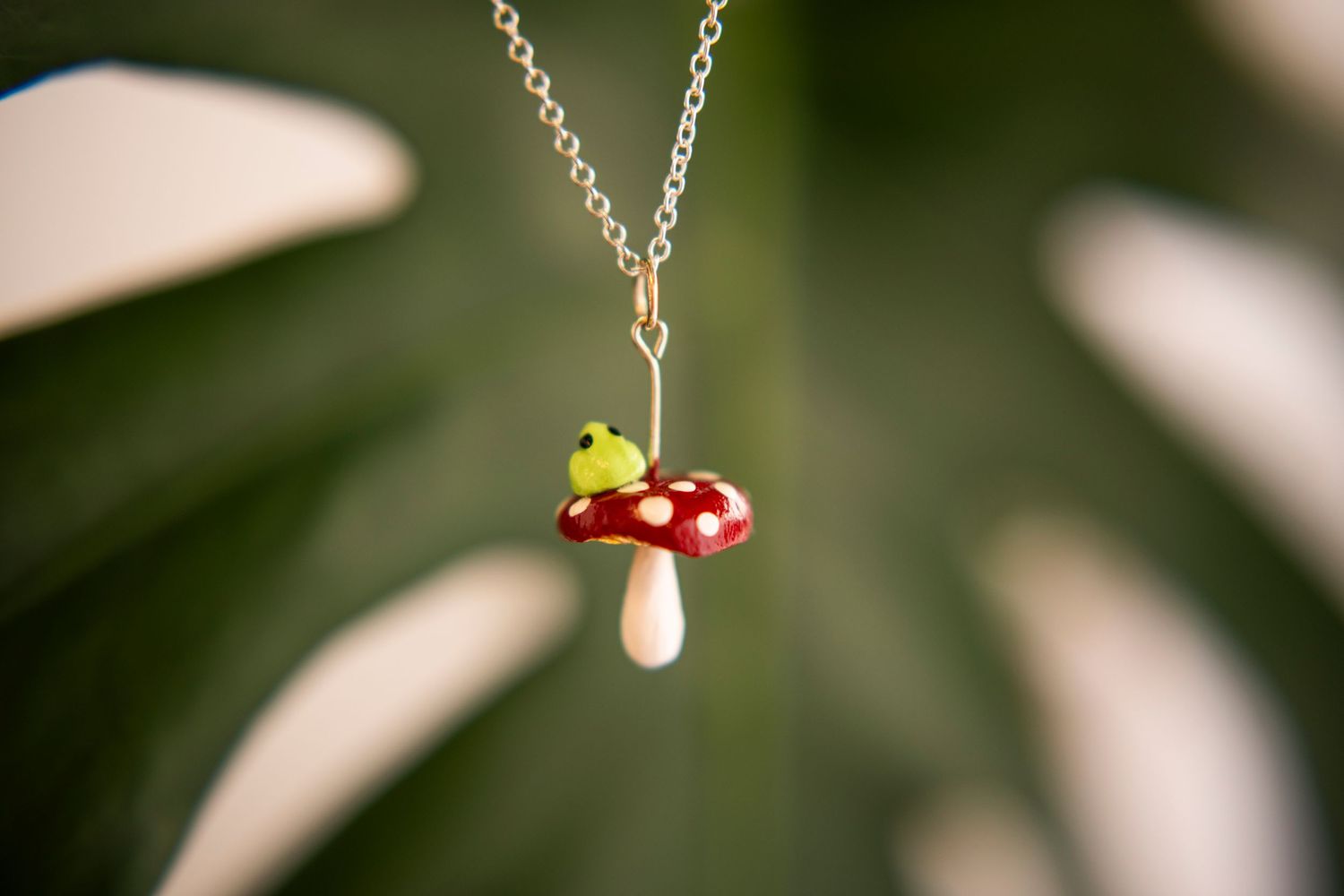 A delicate silver necklace featuring a small pendant charm of a red and white spotted toadstool mushroom.