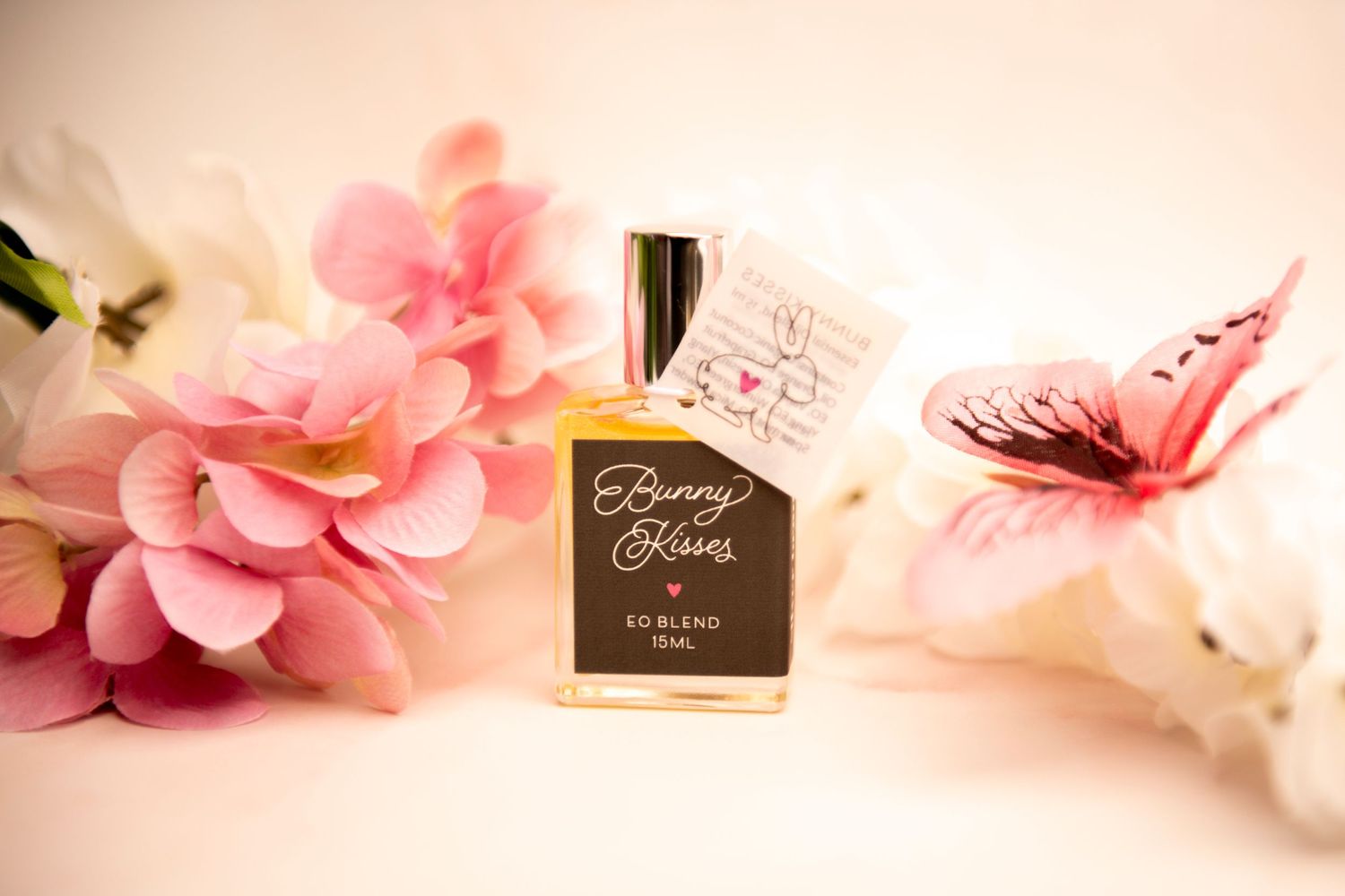 A perfume bottle labeled 'Petite Paris' sits between pink floral decorations and a pink butterfly on a soft background.