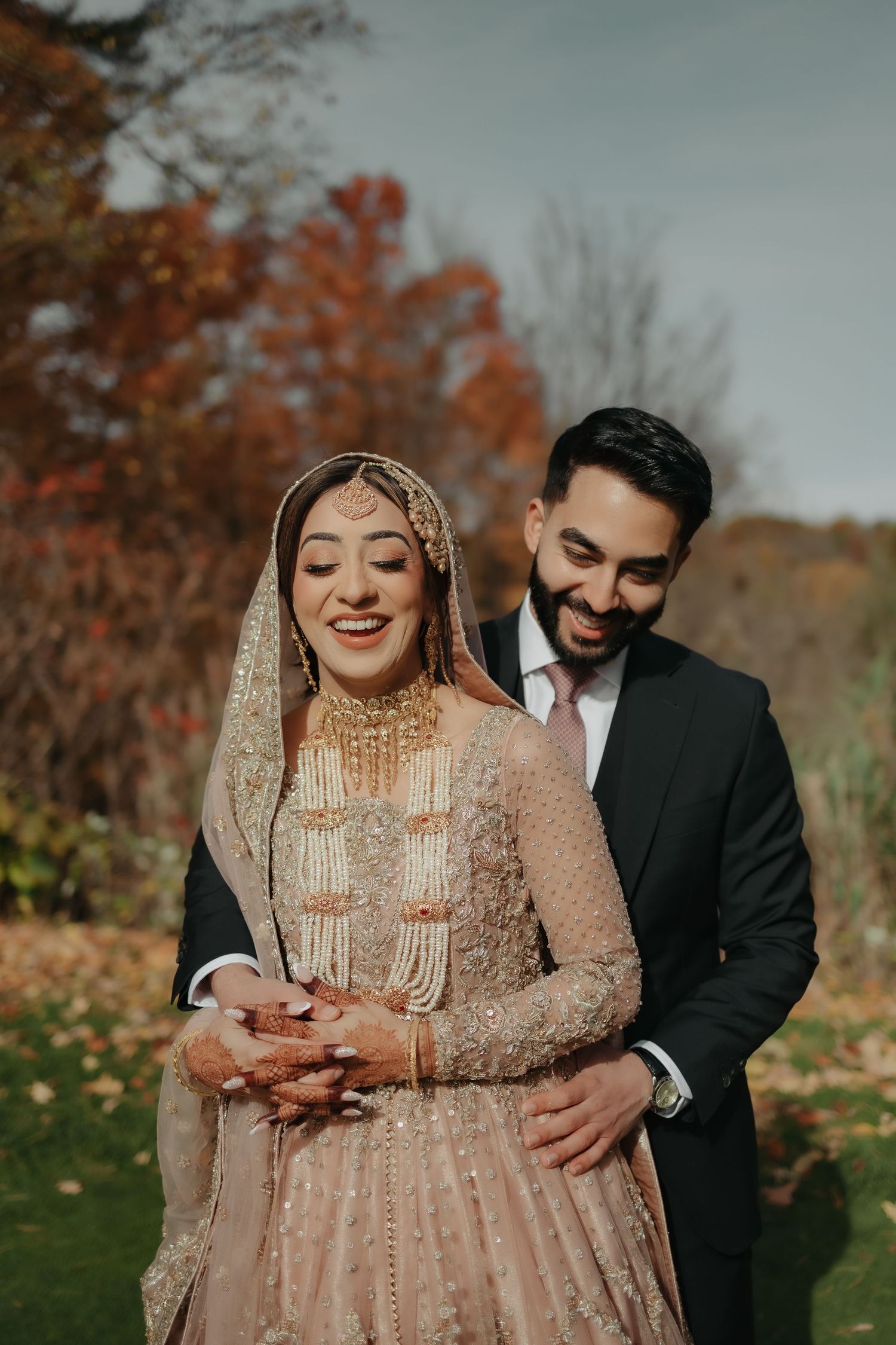 A couple embraces outdoors during autumn with vibrant fall foliage in the background.