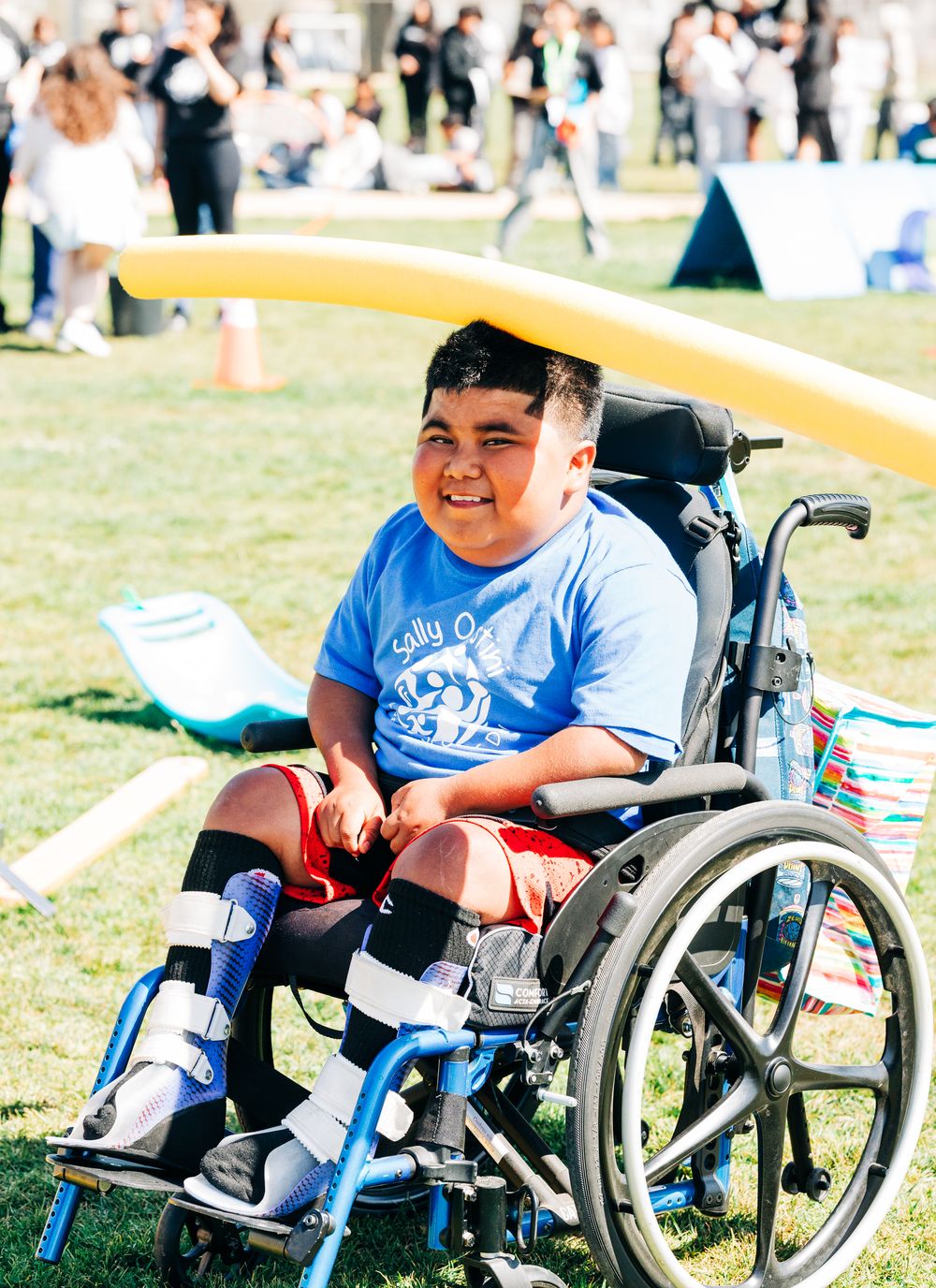 Little boy in a wheelchair with a pool noodle on his head at a field day event, Santa Maria, CA