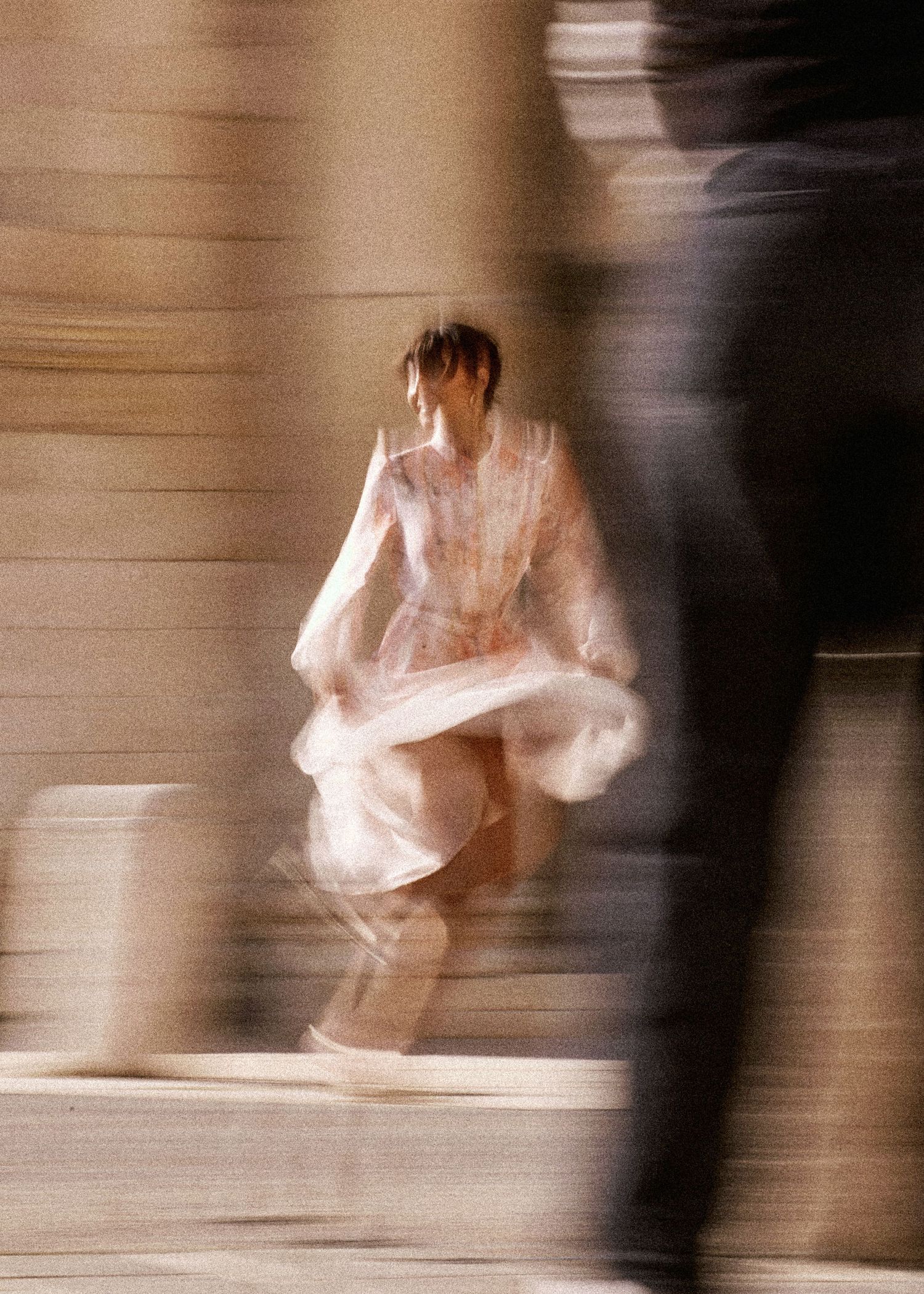 Blurred motion shot of a dancer in a flowing white dress performing on stairs.