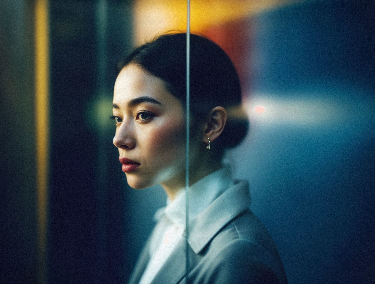 A profile portrait in moody lighting showcases someone in a white collar shirt against a blue background.