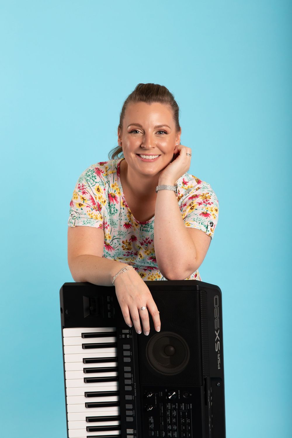 Portrait of musician posing with keyboard against turquoise background.