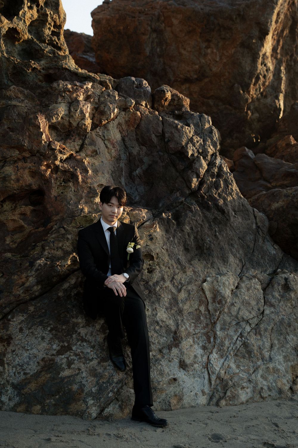Silhouetted figure in dark suit stands against dramatic rocky cave wall backdrop at sunset.