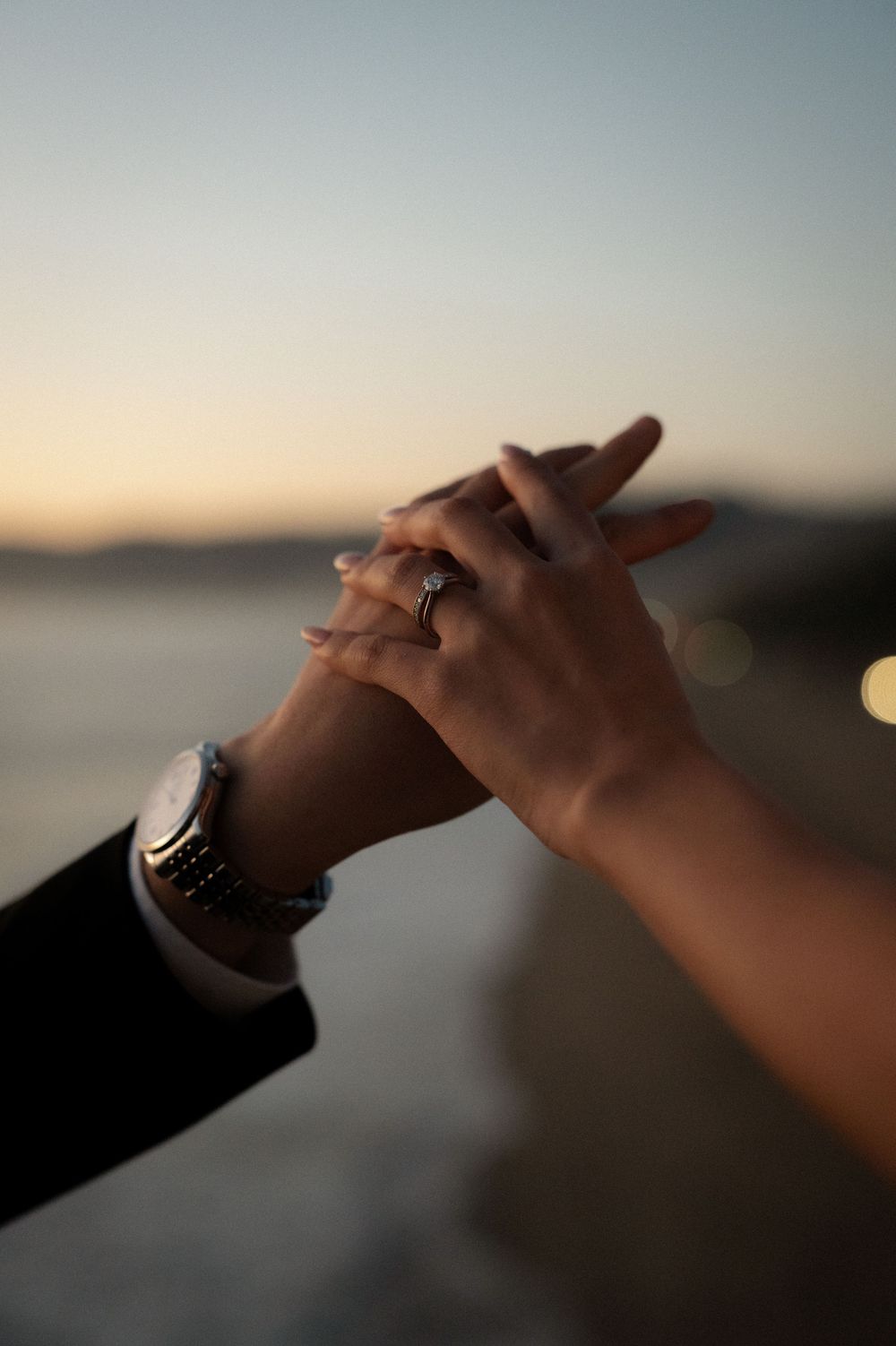 Silhouetted hands clasped together against a blurred sunset sky background create a romantic moment.