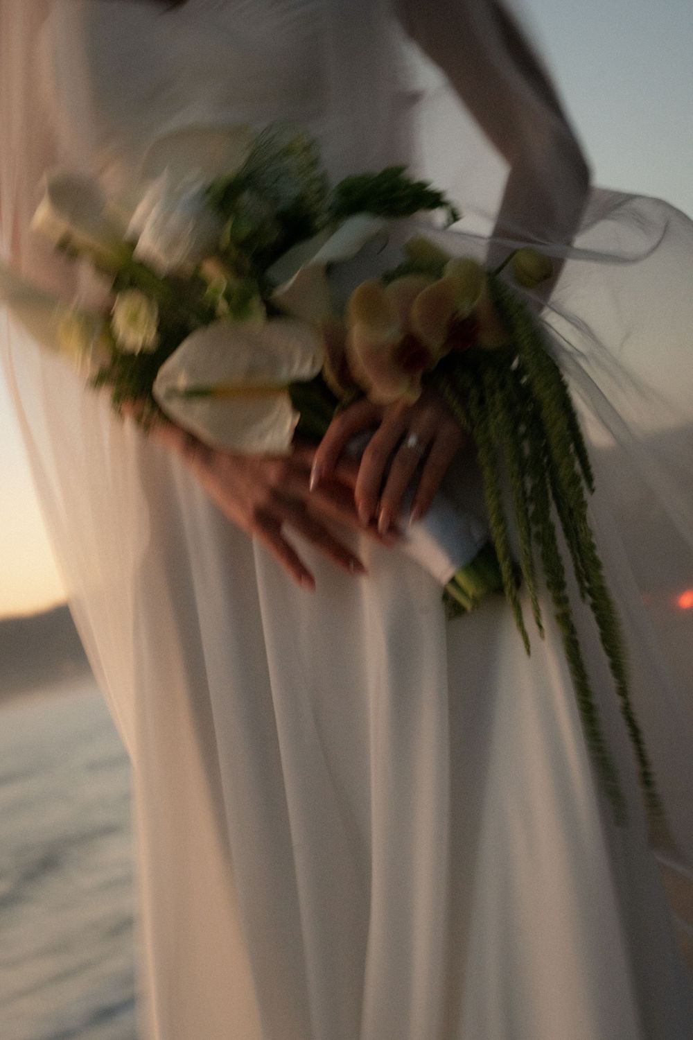 Close-up details of a white wedding dress and cascading greenery bouquet at golden hour by the malibu ocean.
