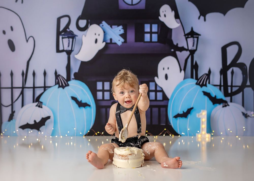 Halloween party table setting with spooky decorations, cupcakes and string lights against a haunted house backdrop.