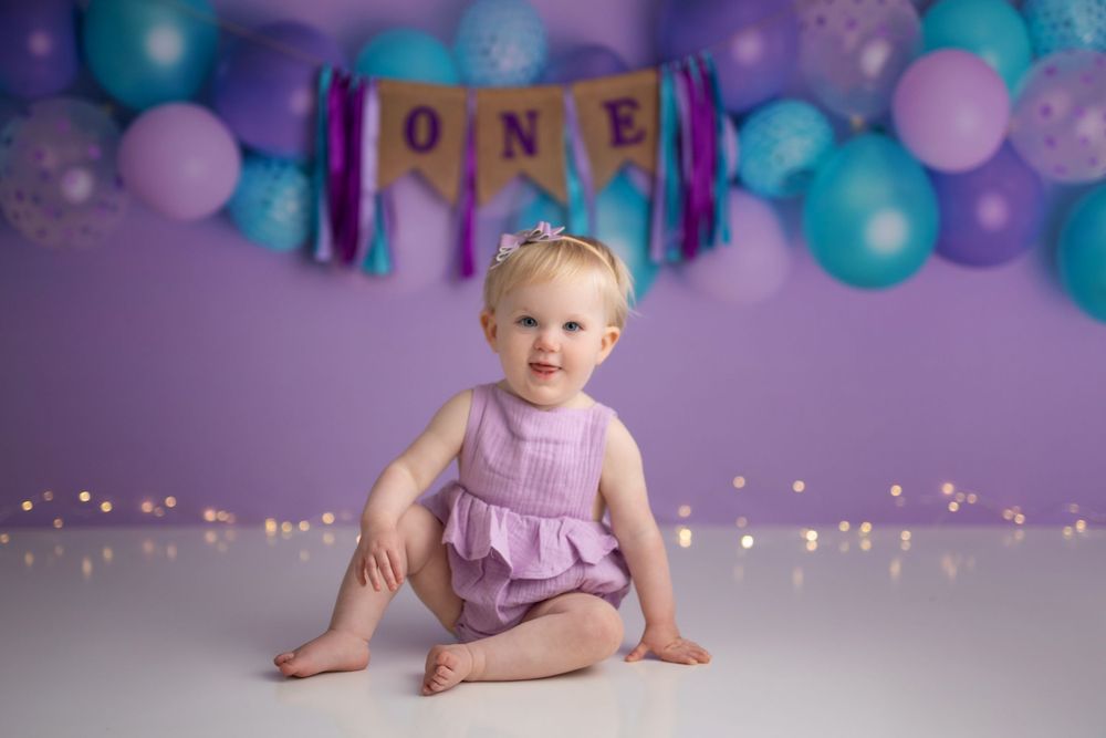 Purple and teal balloon arch first birthday setup with sparkly lights.