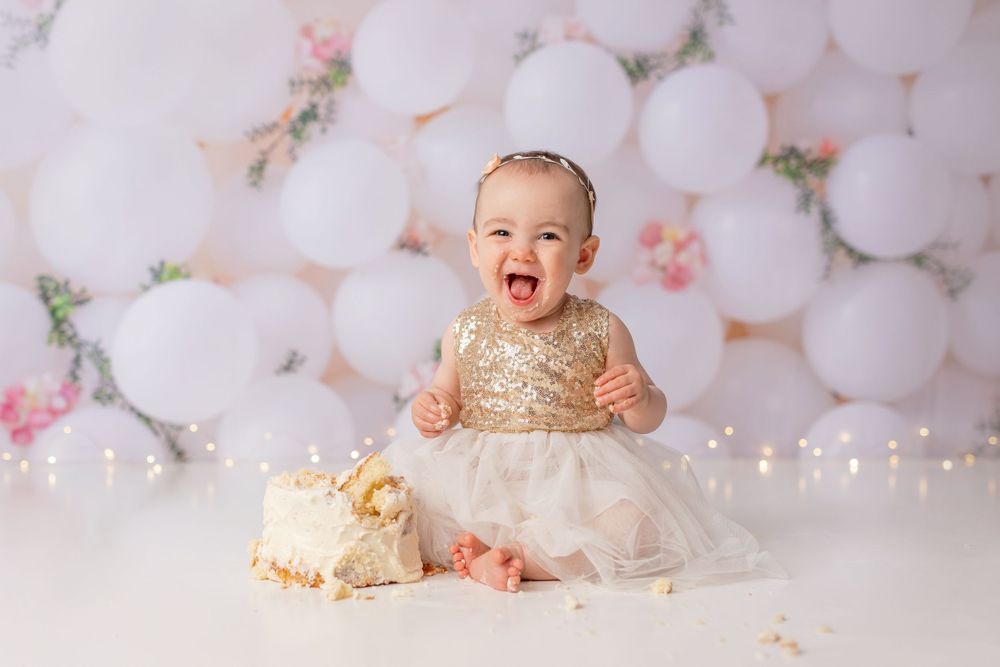 Elegant white balloon arch backdrop with gold and white cake smash setup.