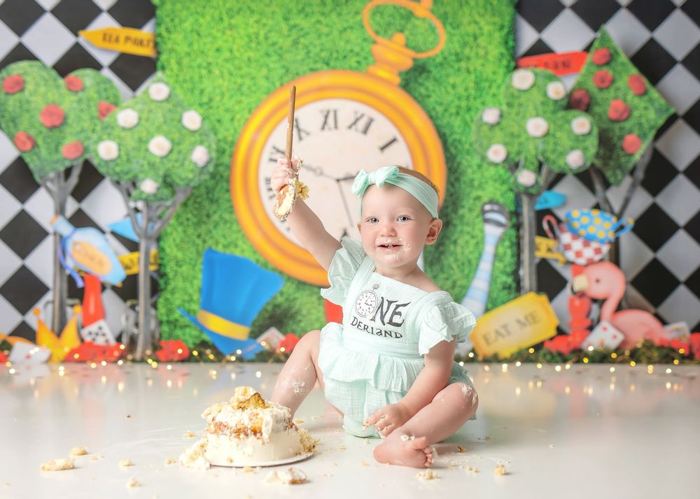 Whimsical Alice in Wonderland themed first birthday party setup with oversized clock, checkerboard backdrop and cake smash.