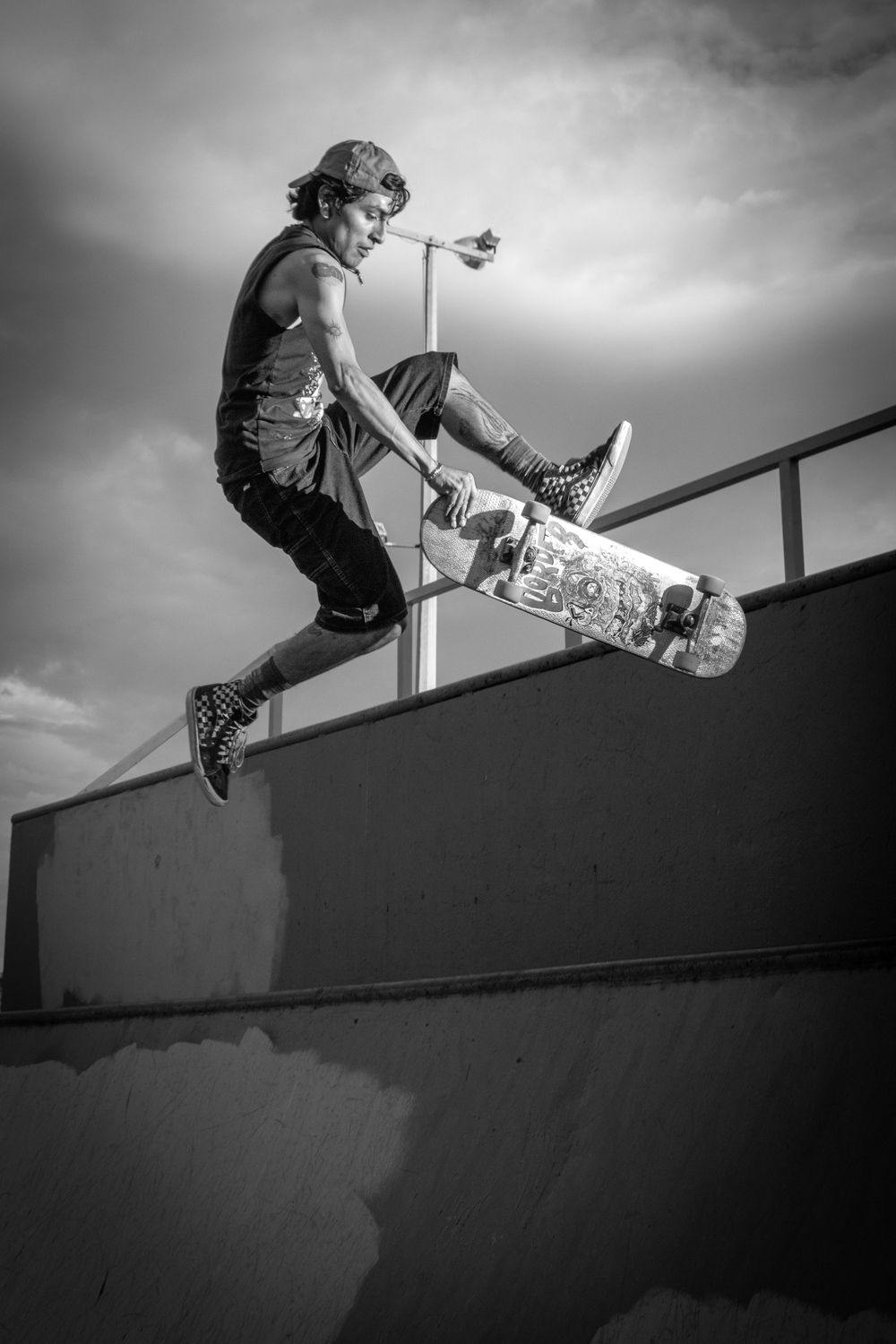 Black and white photo of a skateboarder performing a trick on a concrete ramp under cloudy skies.