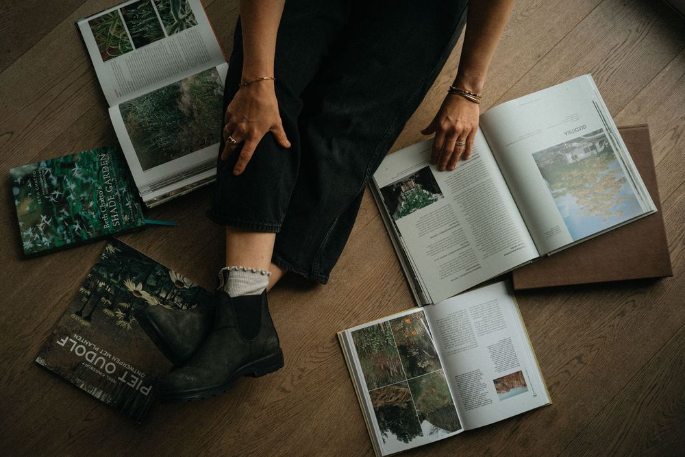 Overhead view of hands flipping through photo albums and books on a wooden floor.