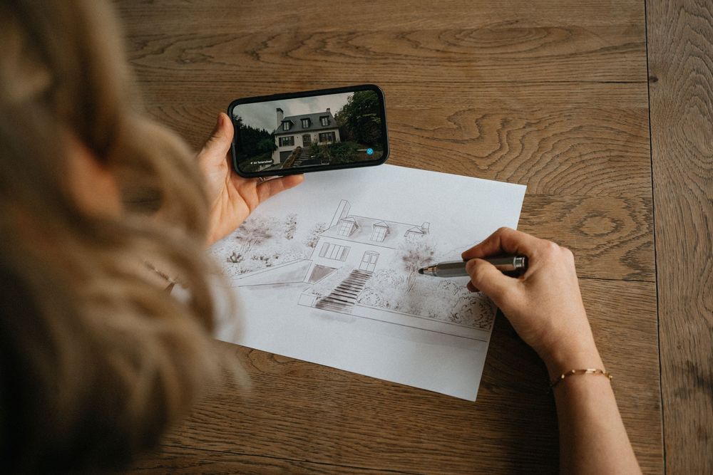 Someone holding a smartphone and taking notes on paper while working at a wooden desk surface.