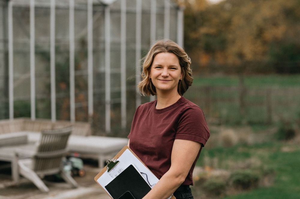 Professional photographer in burgundy shirt smiles while working outdoors with camera and laptop during autumn session.