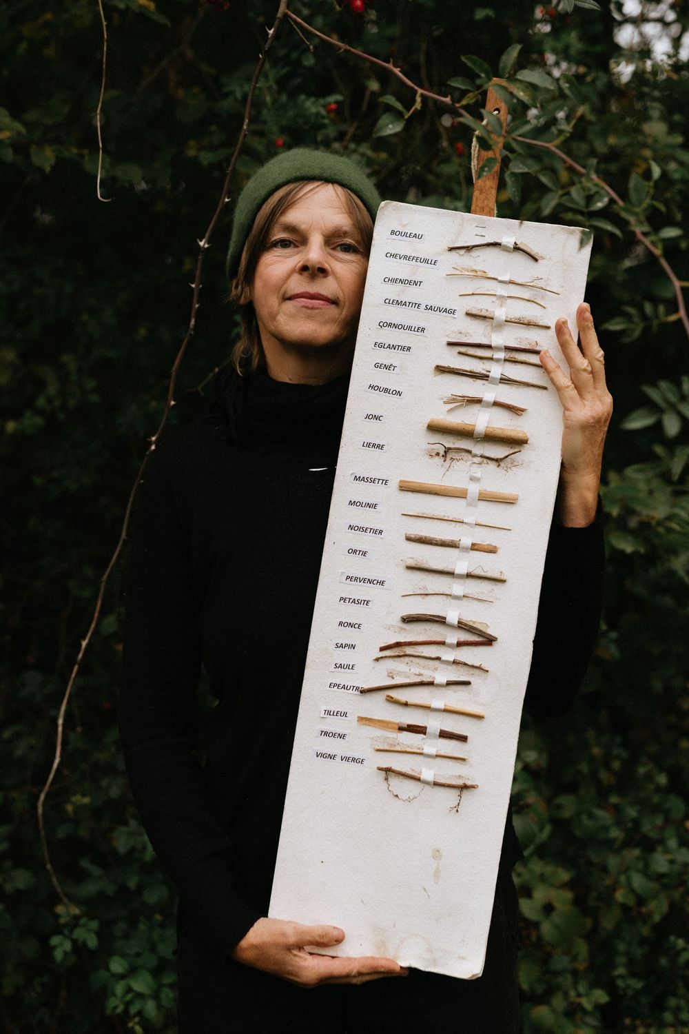 A person in black holds a large display board showing various dried and preserved fish specimens against a dark foliage background.