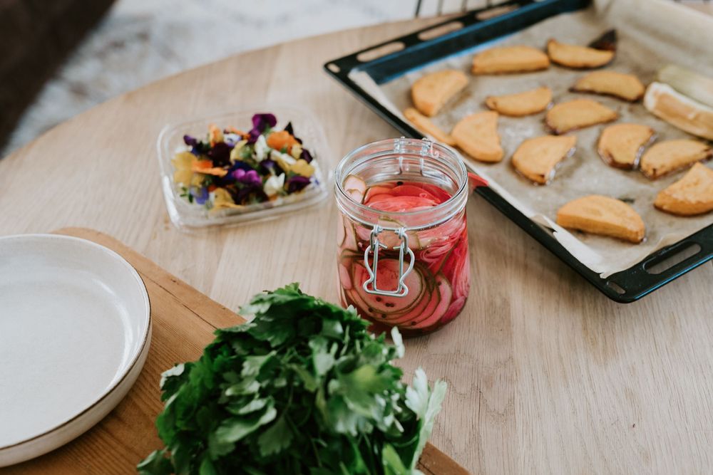 Kitchen scene with fresh herbs, red drink in jar, and baked cookies on tray.