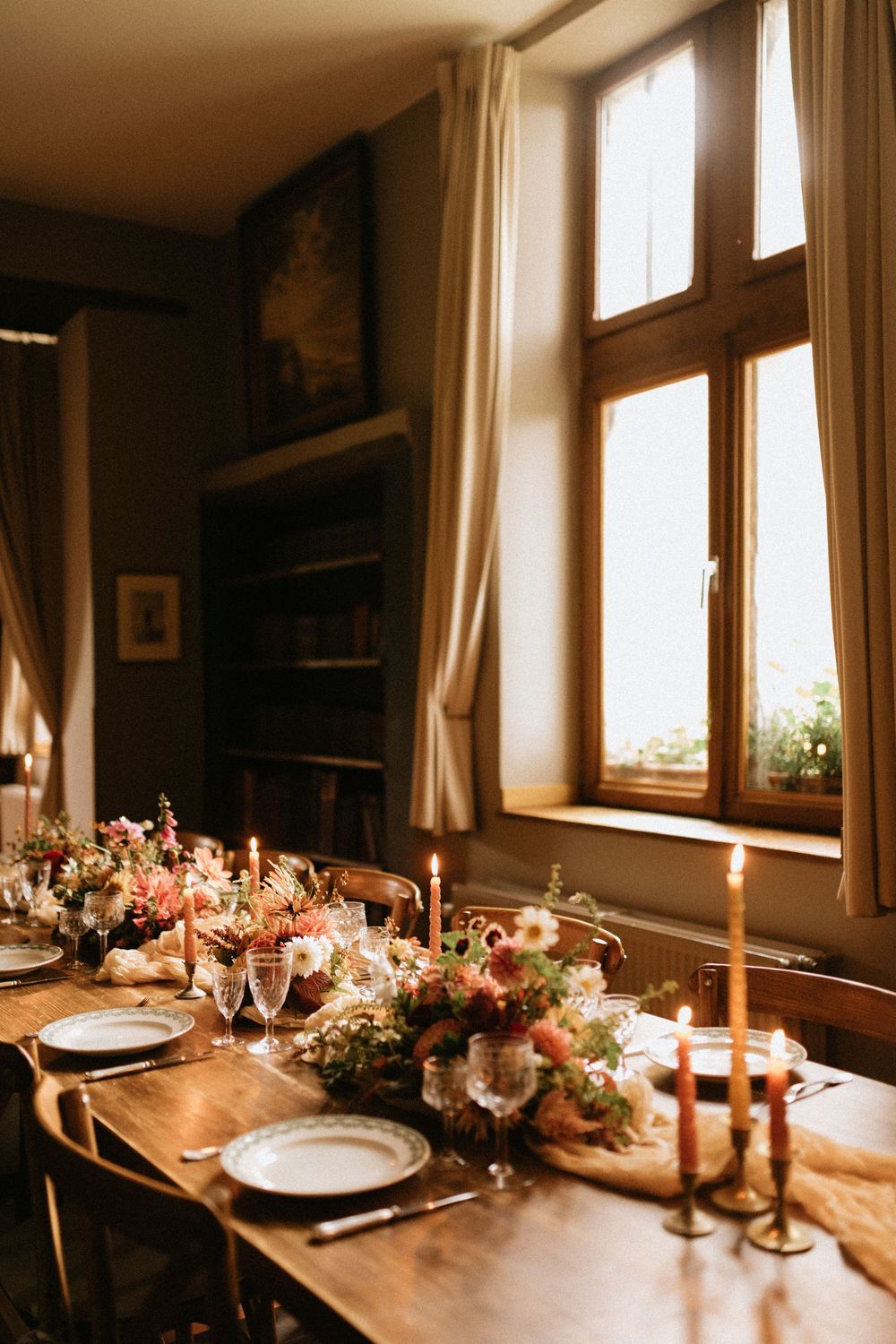 Elegant table setting with floral centerpieces and candles in warm sunlit room.