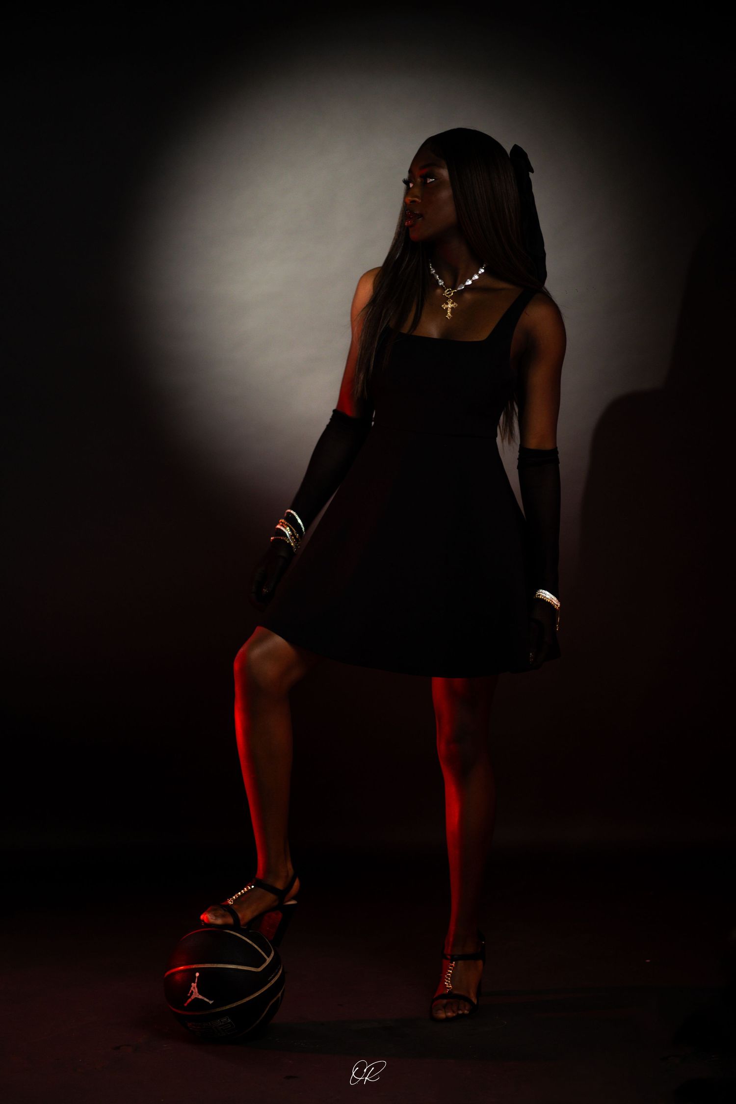 A silhouetted figure in a black dress poses with dramatic lighting against a dark background with glowing red accents.