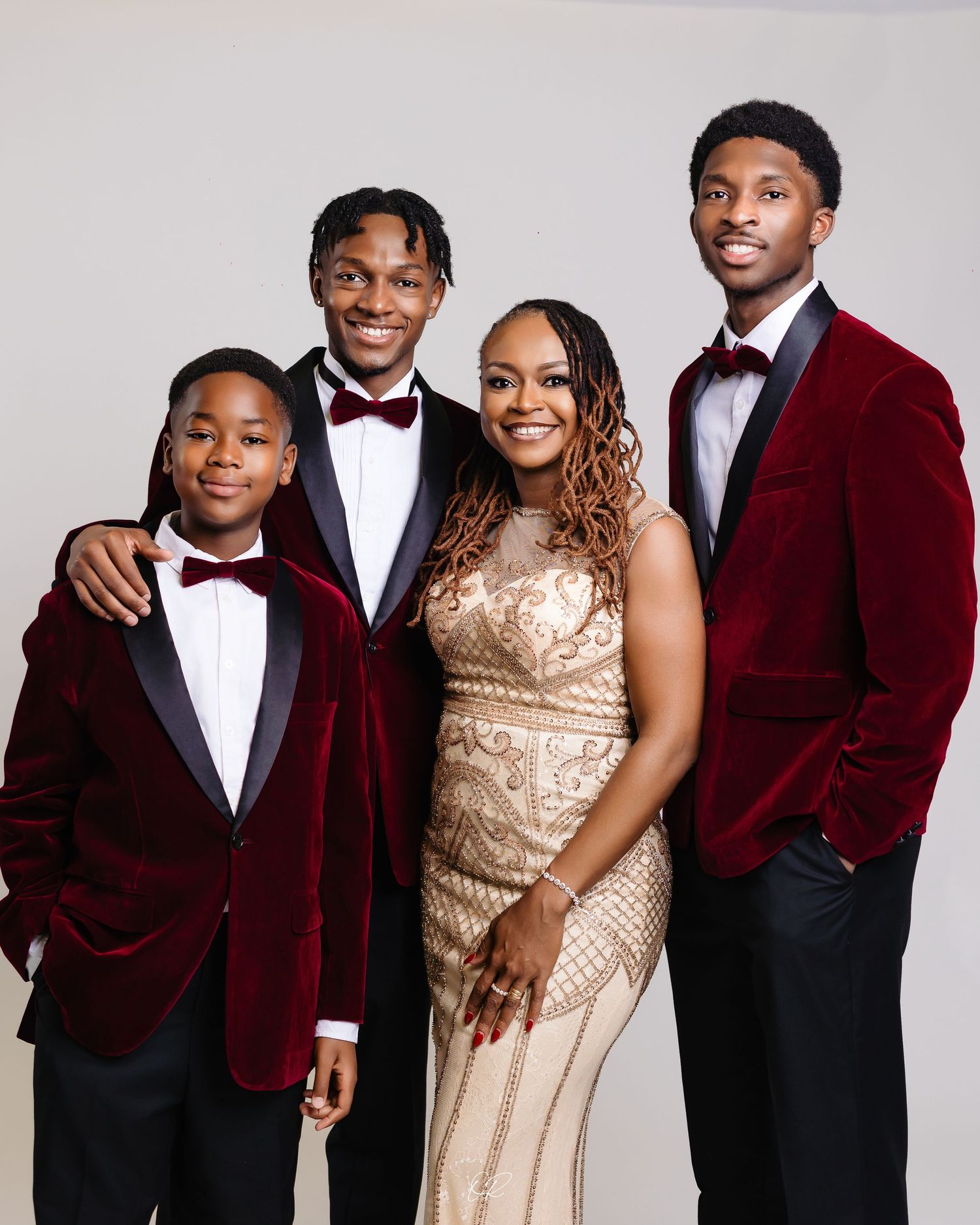 Formal group portrait with three people in burgundy velvet tuxedos and one person wearing a sparkly champagne-colored gown.
