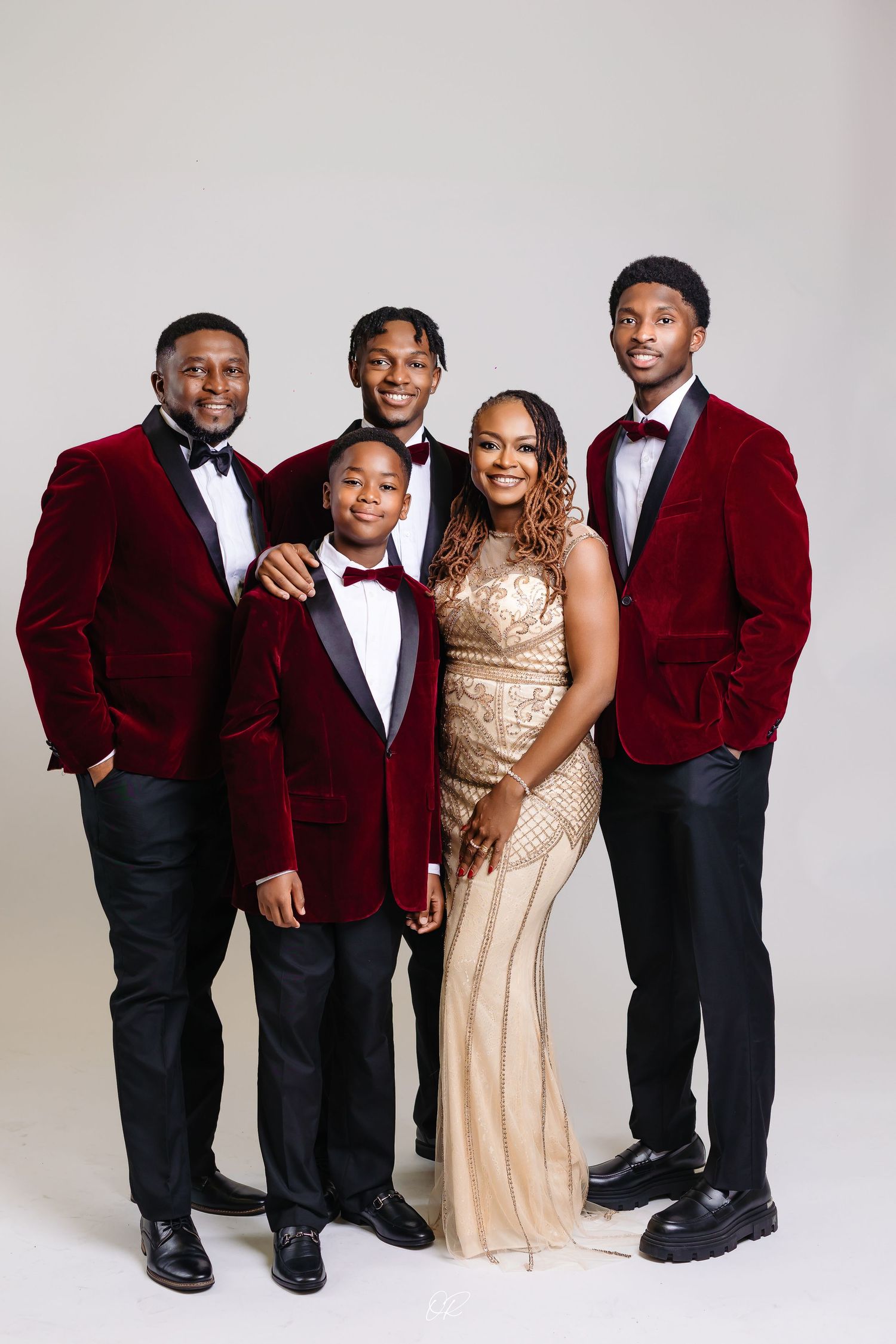 A formal group photo featuring four people in red velvet blazers and bowties with one person wearing a champagne gown.