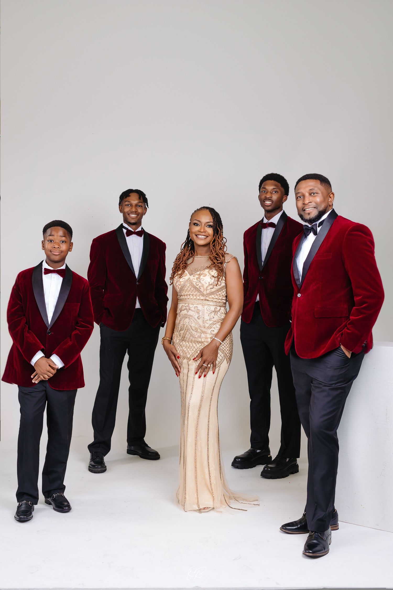 A formal group portrait featuring people in elegant attire including red velvet tuxedos and a champagne-colored gown.