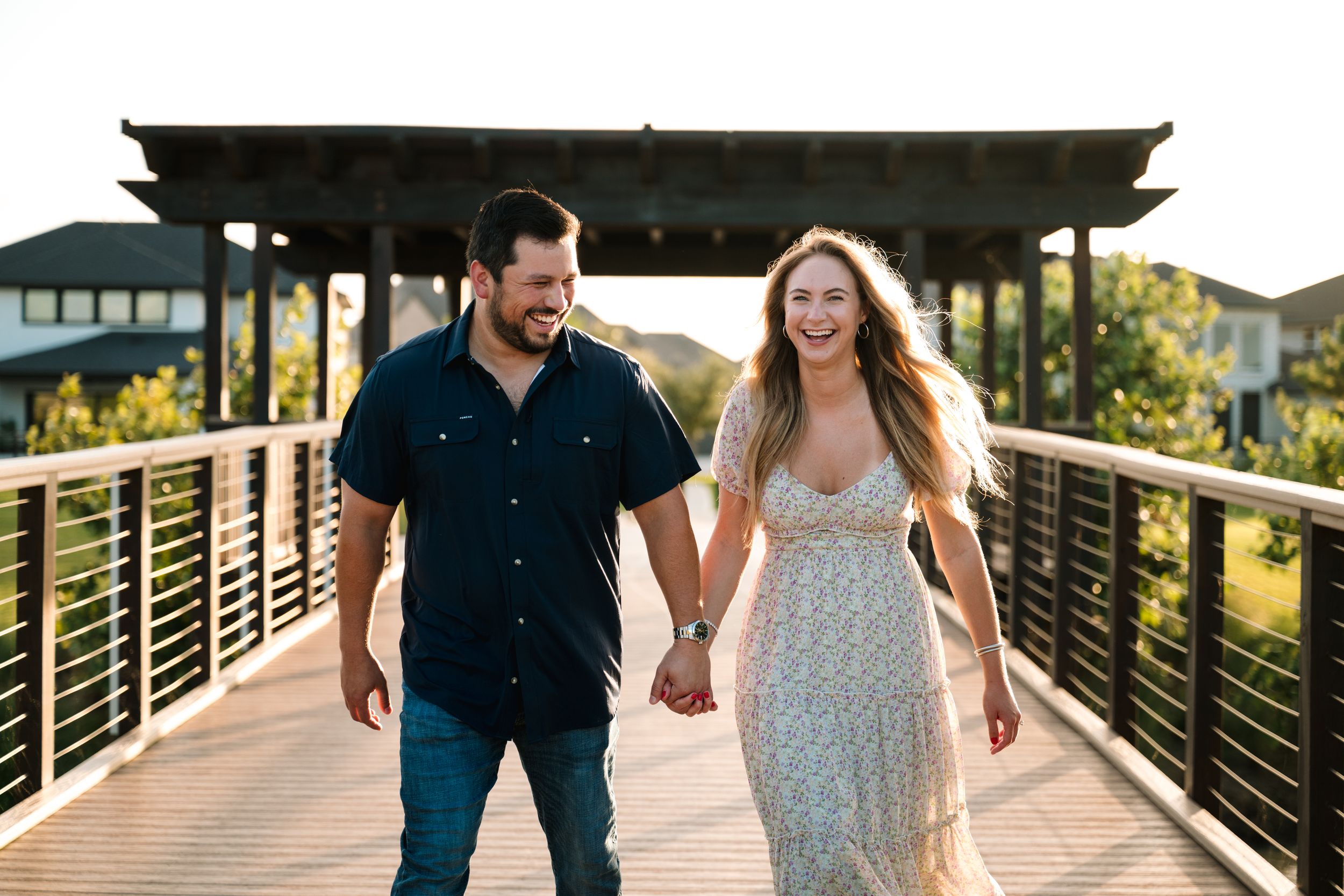 Couple walks together on a wooden bridge during sunset photoshoot.