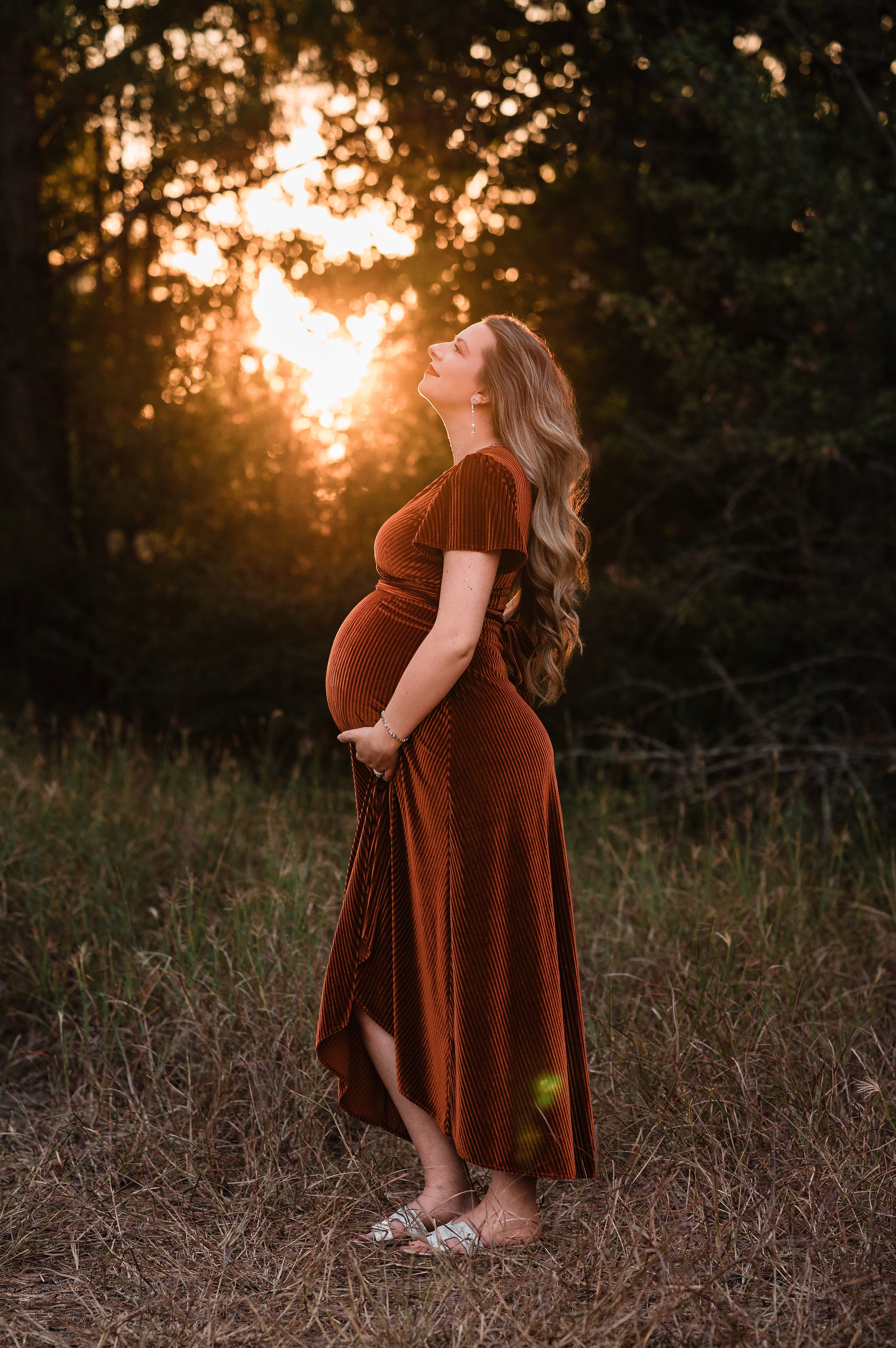 A person in a rust-colored velvet dress stands in a golden field at sunset creating a dreamy autumn atmosphere.