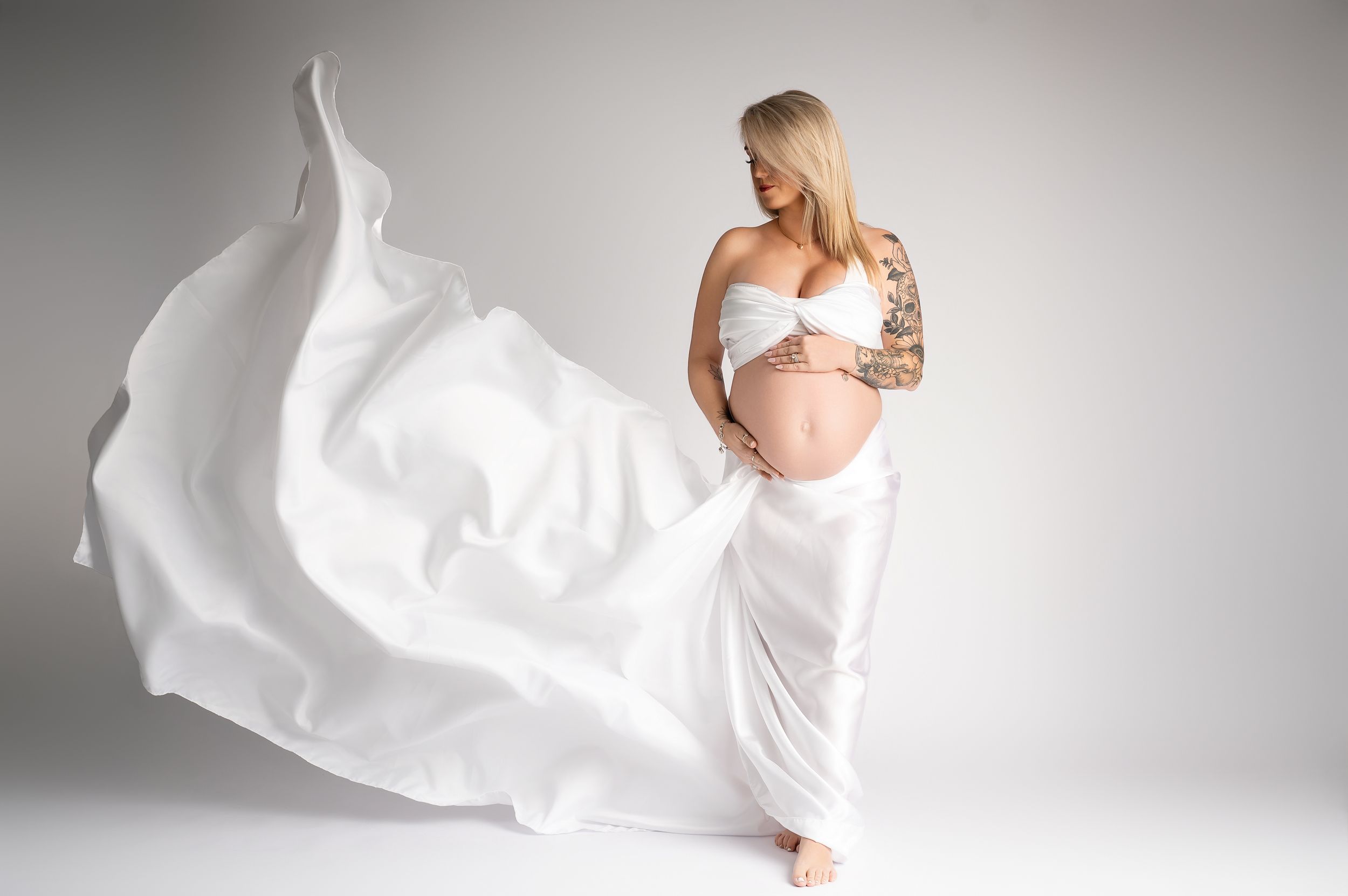 A flowing white fabric creates an ethereal and dreamy effect against a light gray background in this artistic photograph.