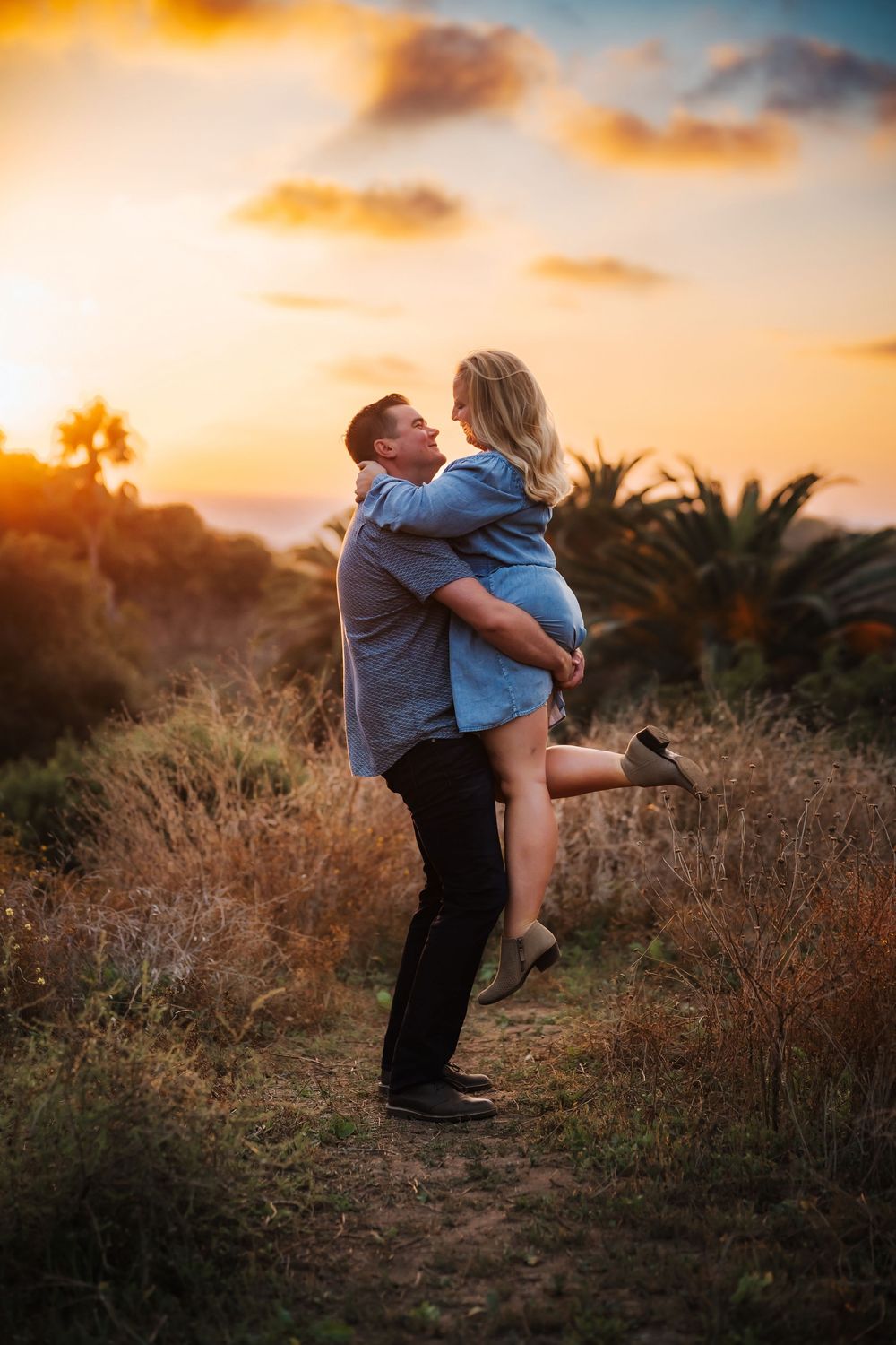 A couple shares a romantic embrace during golden hour sunset in a rustic outdoor setting.