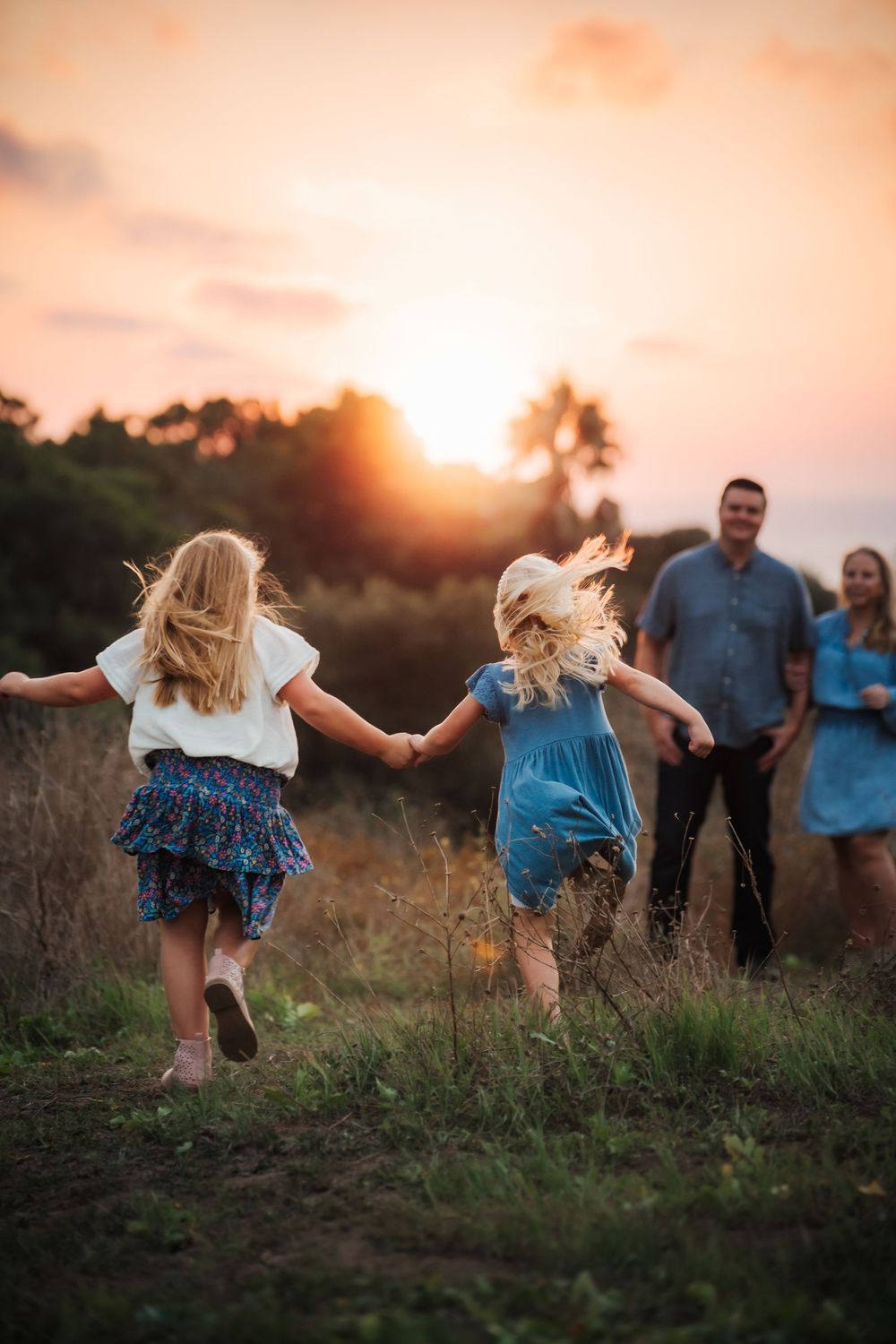 Silhouettes of people walking in a field at sunset while children run ahead playfully.