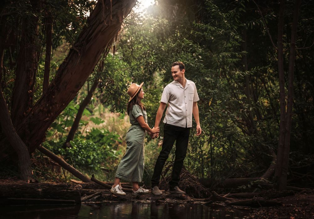 A couple enjoys an intimate moment in a sunlit forest setting during their engagement photo session.