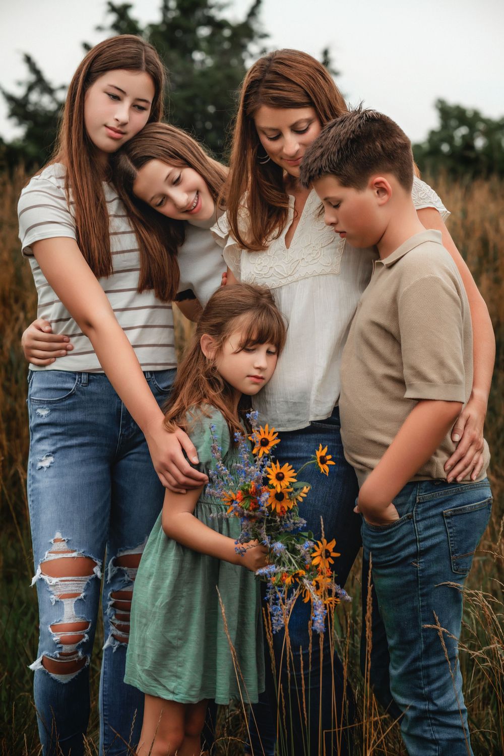 A family stands together in tall grass, with sunflowers adding a pop of yellow to their intimate outdoor portrait session.