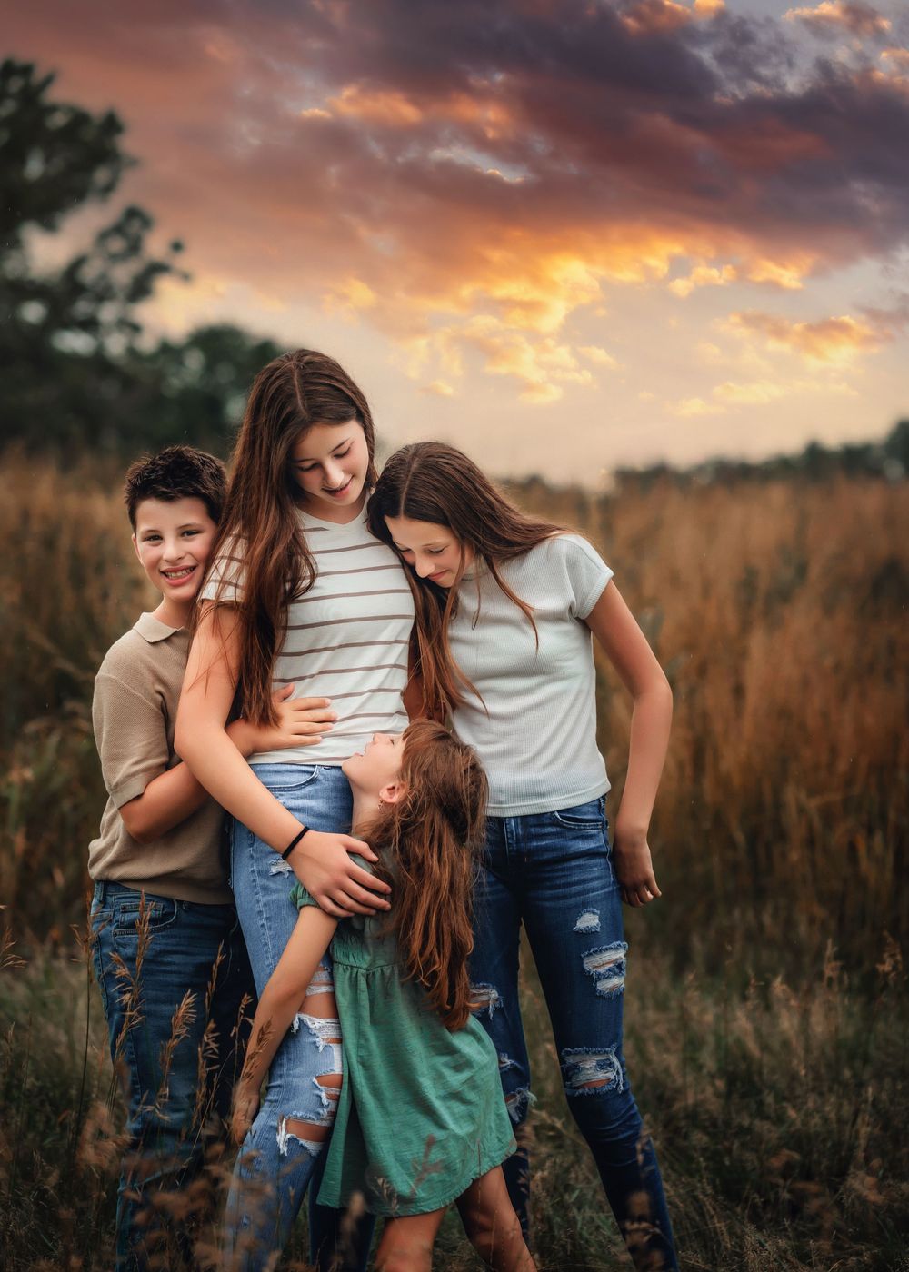 A group embraces while standing in a golden wheat field at sunset with dramatic orange clouds in the sky.