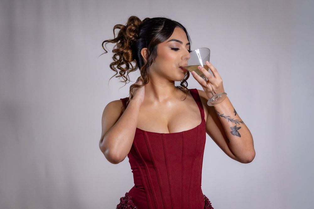 Woman in burgundy formal dress poses elegantly against gray backdrop in fashion photoshoot series.