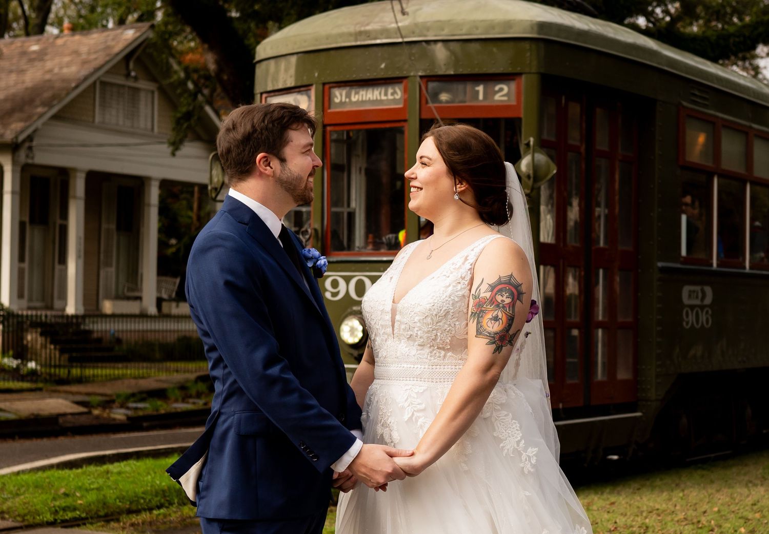 Newlywed couple holds hands and smiles at each other in front of a vintage red streetcar.