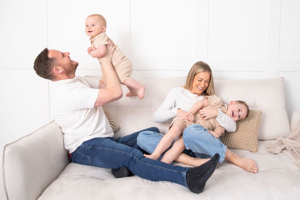 Happy family with two babies playing on a cozy white sofa in a bright living room.