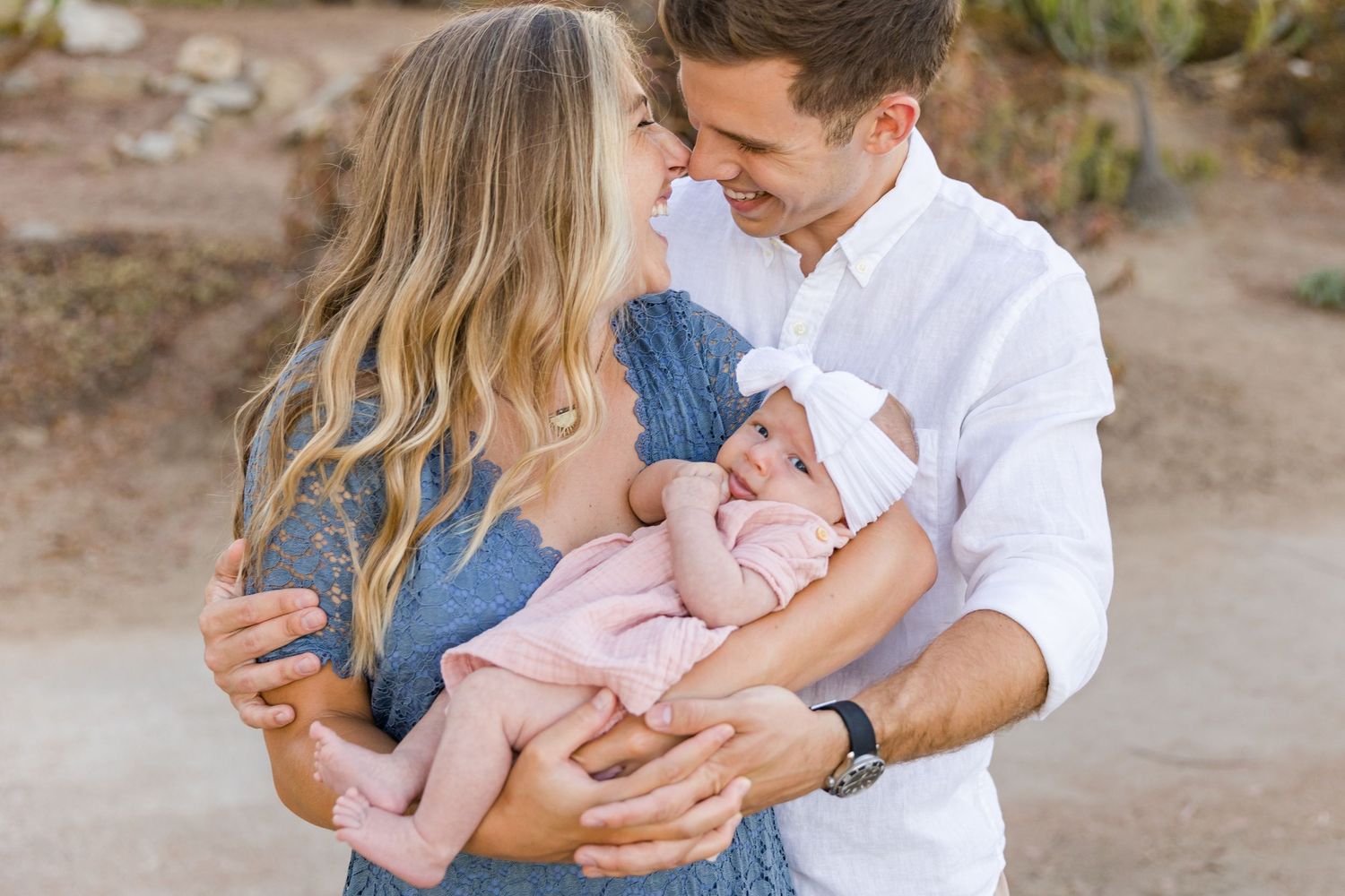 An intimate outdoor family moment with a newborn baby in pink being cradled between two parents.