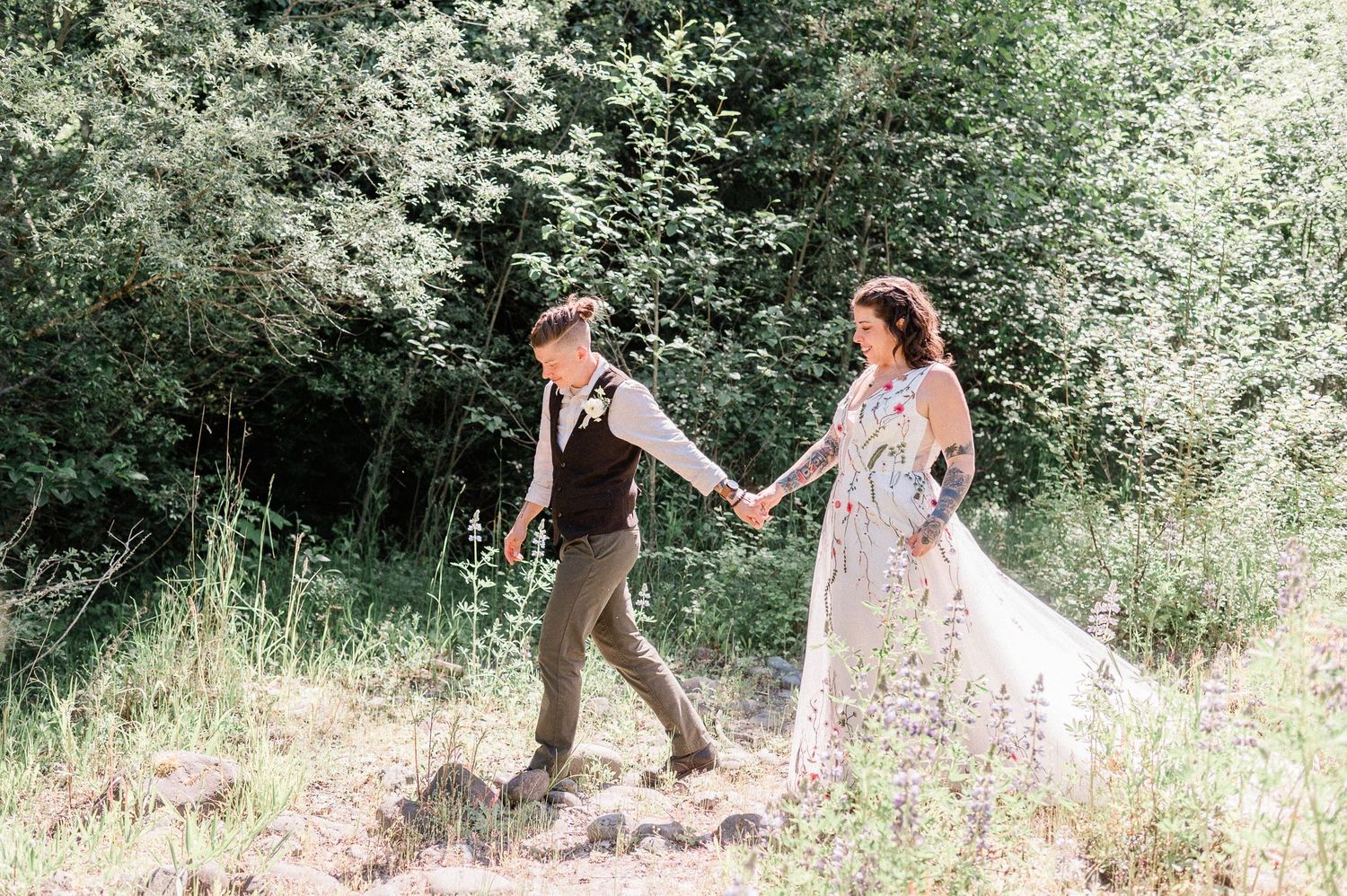Two brides walking hand in had through flowers on a sunny day in Washington