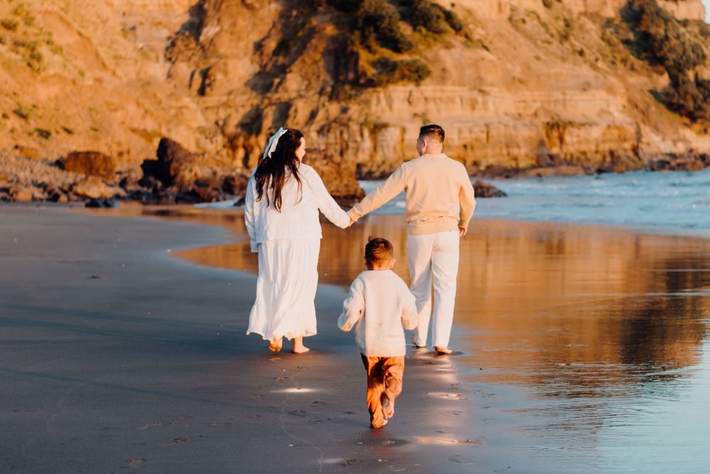 A family walking together on a wet sandy beach with cliffs in the background at golden hour.