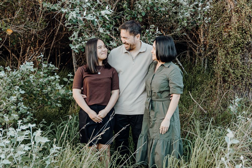 Three people standing together in tall grass and flowering bushes during a photo session.