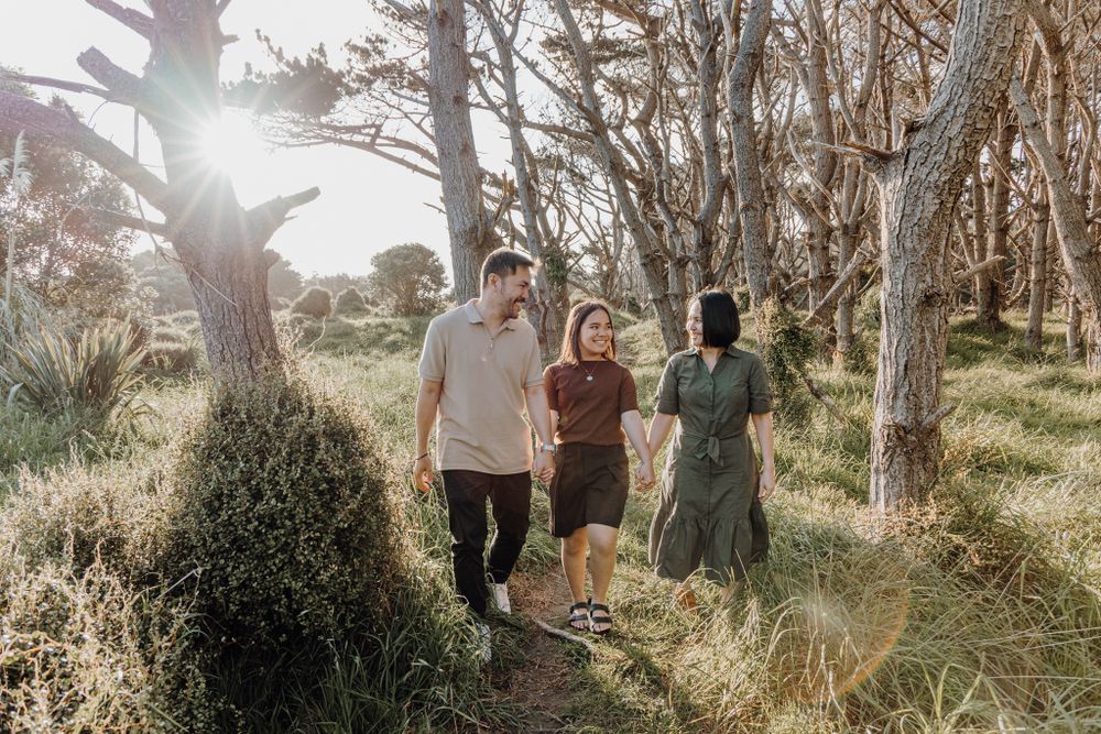 Three people walking together on a sunlit forest path surrounded by tall trees.