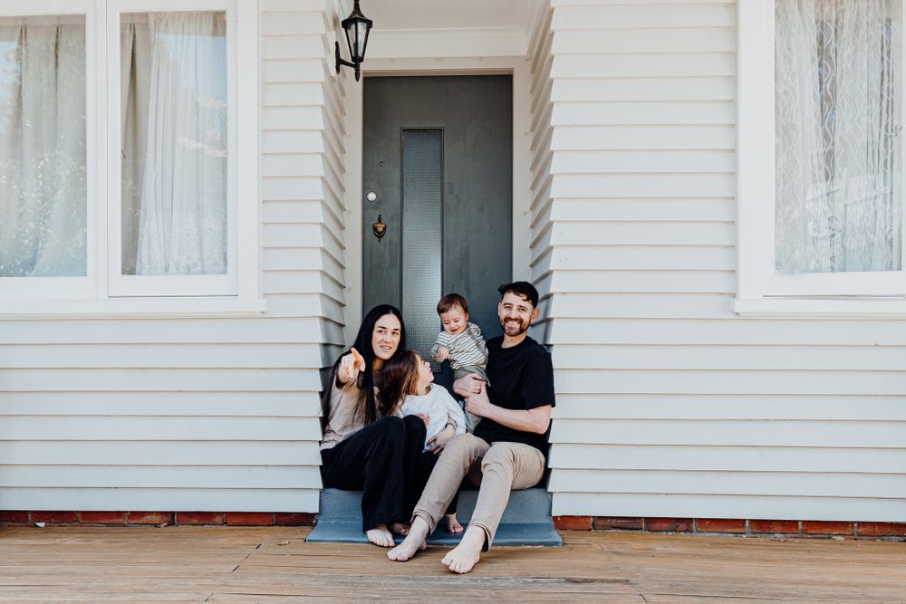 Family sitting together on white porch steps of a traditional house with siding.