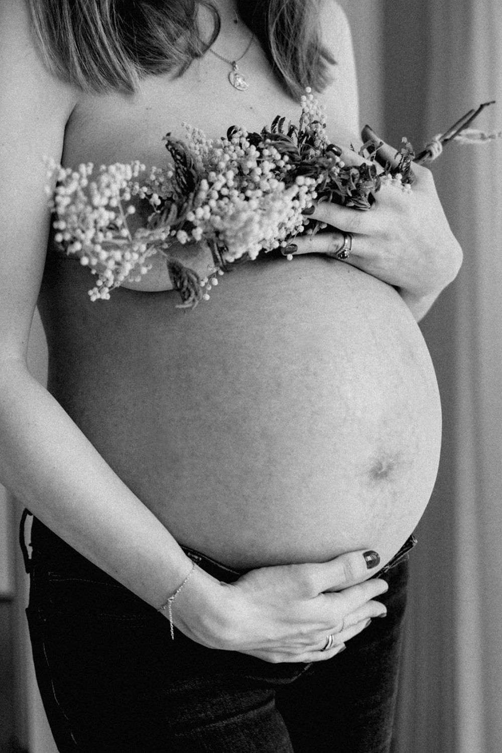 photo du ventre d'une femme enceinte portant un bouquet de mimosa pour cacher sa poitrine