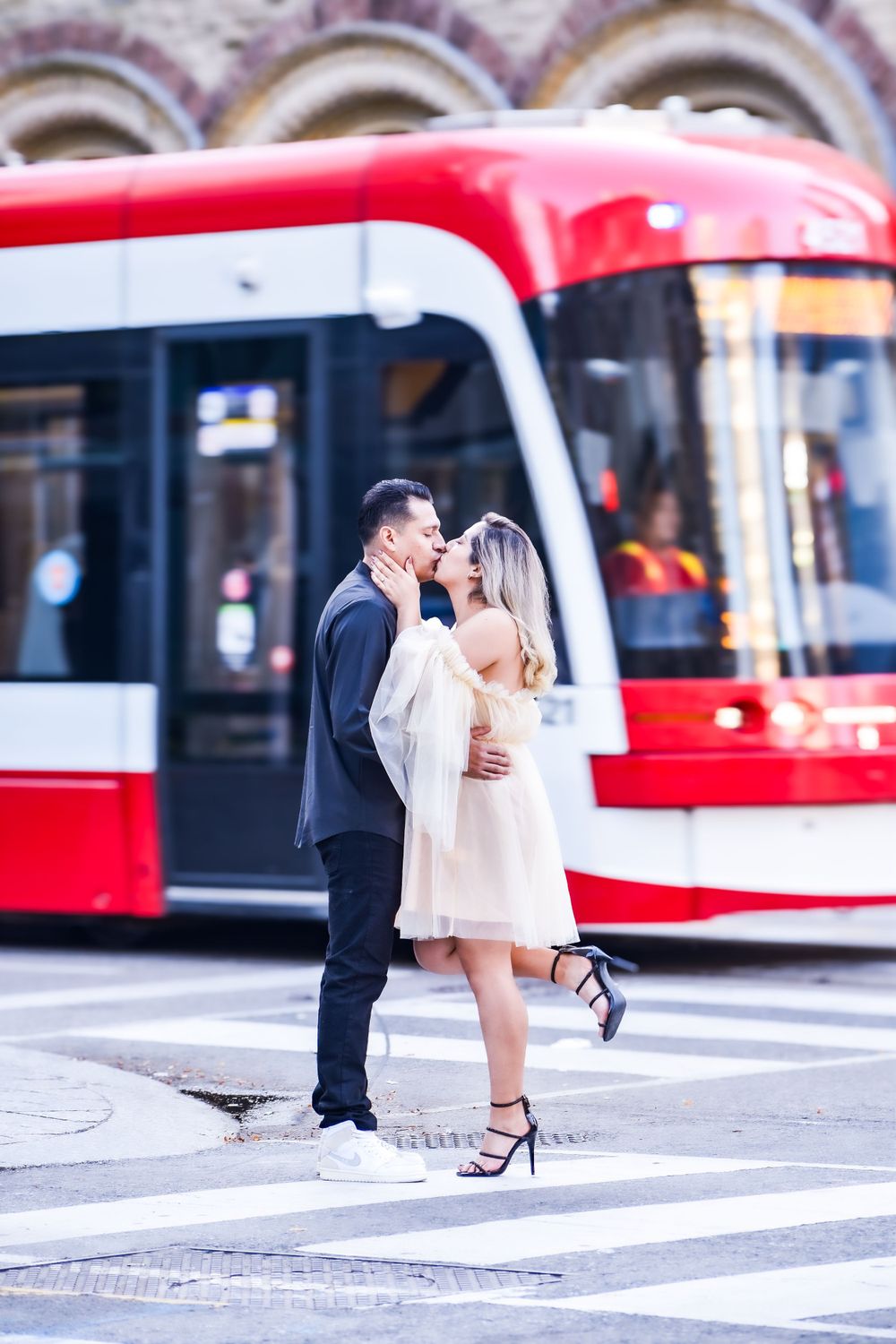 Couple sharing a kiss on a crosswalk with a red city tram in the background. Toronto GTA