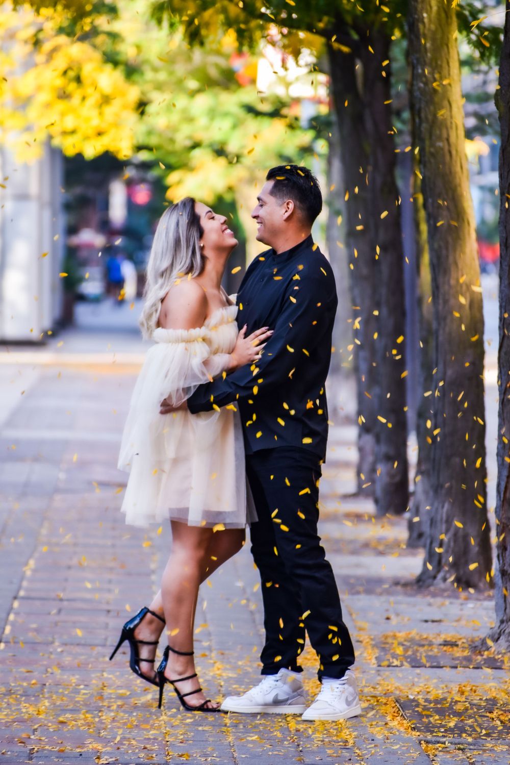 Couple embracing joyfully under falling golden confetti on an autumn street. Toronto GTA