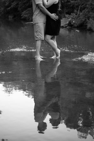 Black and white photo of couple standing in water with reflection creating mirror effect.
