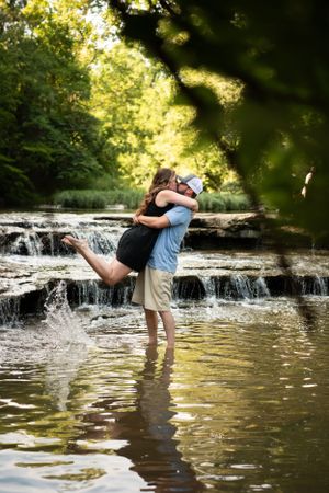Romantic couple embracing in shallow waterfall during summer photoshoot.