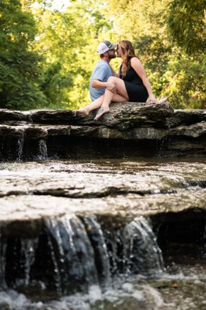 Couple sitting together on rocky waterfall ledge in nature setting.