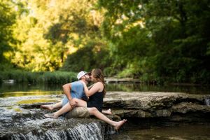 Couple relaxing on rock formation near flowing water in lush forest setting.