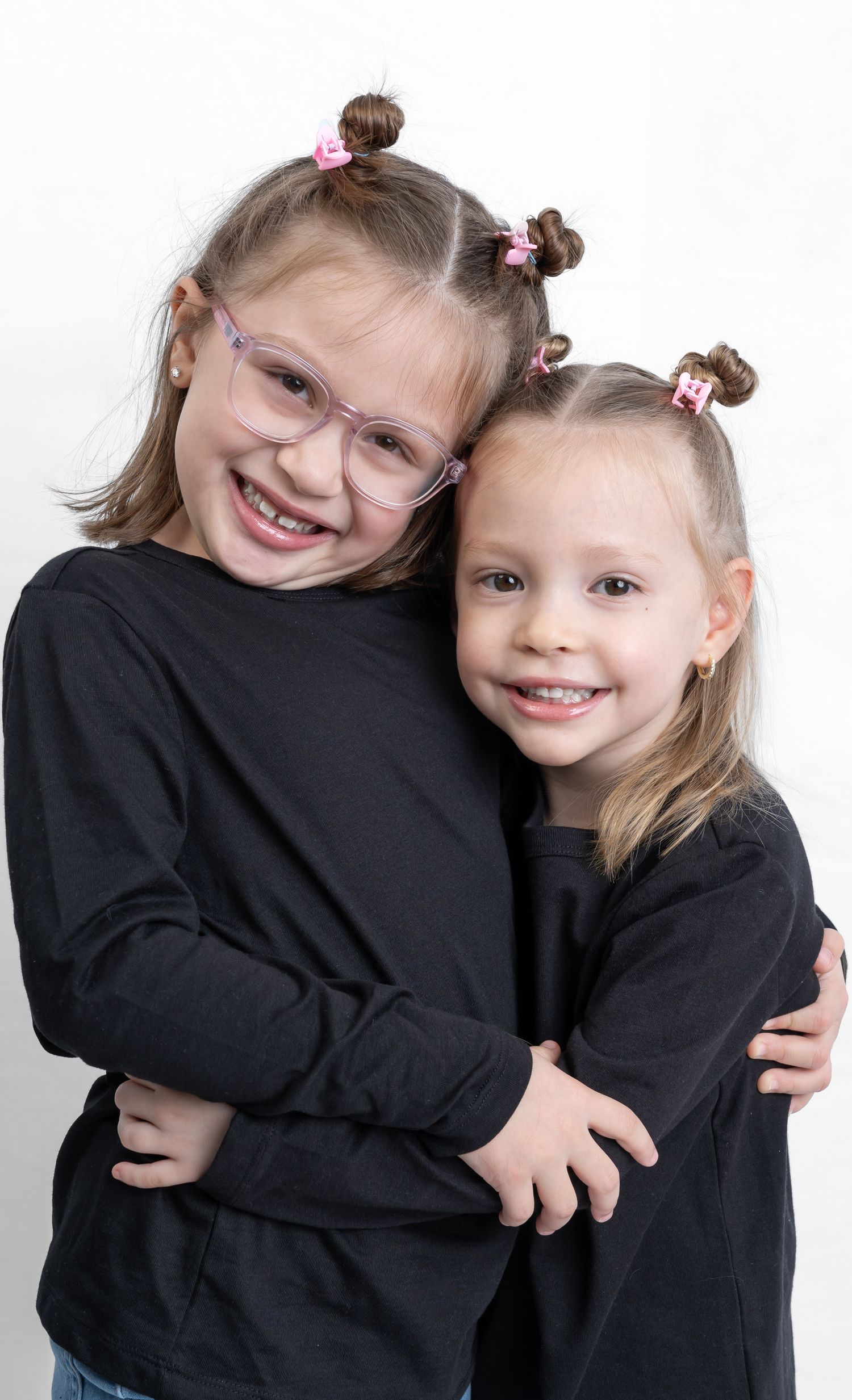 Studio portrait featuring matching black sweaters and playful hairstyles.